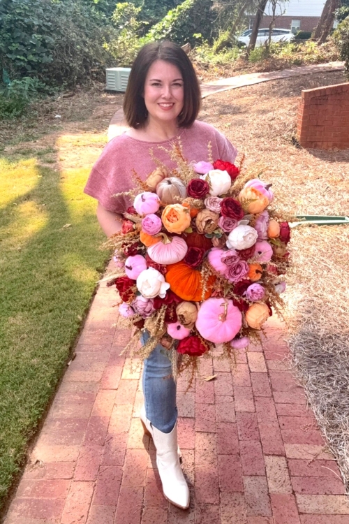 Shop owner holding velvet pumpkin and peony wreath with pink, orange and burgundy florals