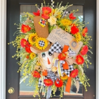Close up of handcrafted scarecrow with pumpkin and floral accents wreath on a door.