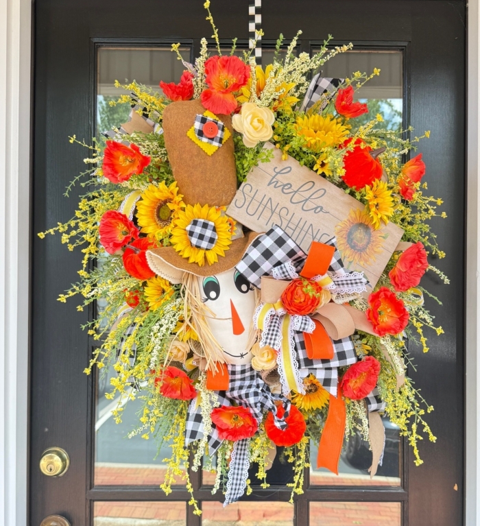 Close up of handcrafted scarecrow with pumpkin and floral accents wreath on a door.