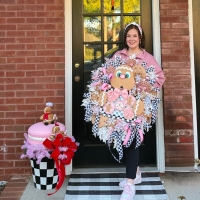 Owner Michelle holding a pink gingerbread cookie wreath against a black door.
