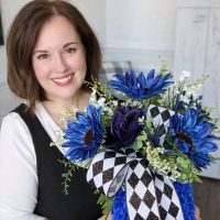 Owner of Wisp & Wonder Designs holding blue sunflower centerpiece with harlequin ribbon.
