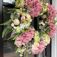 large handmade spring wreath with pink hydrangeas, roses and greenery displayed on front door
