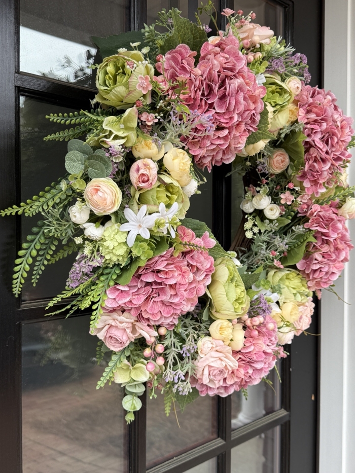 large handmade spring wreath with pink hydrangeas, roses and greenery displayed on front door