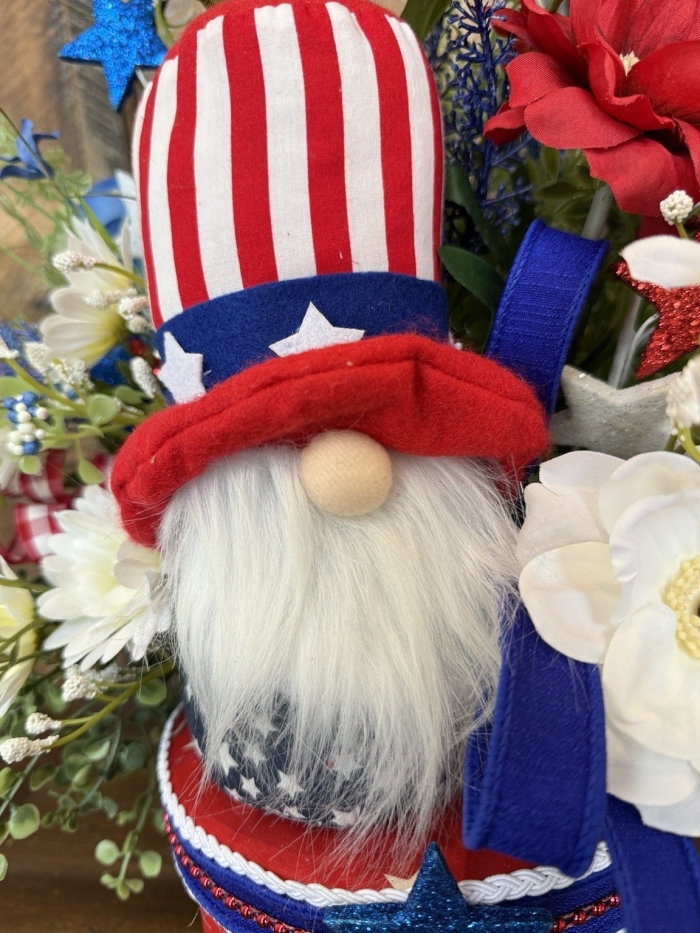 Close up view of the Uncle Sam inspired gnome, showing his striped hat, soft white beard, and surrounding red, white and blue florals