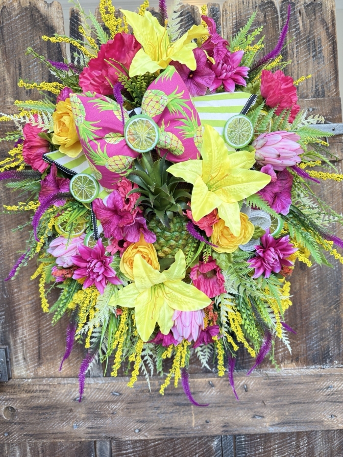 colorful pineapple wreath with bright tropical flowers and handmade bow on rustic door