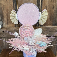 Back view of a whimsical candy centerpiece showcasing oversized candy decorations, pastel swirl lollipops, glitter details and decorative foliage.