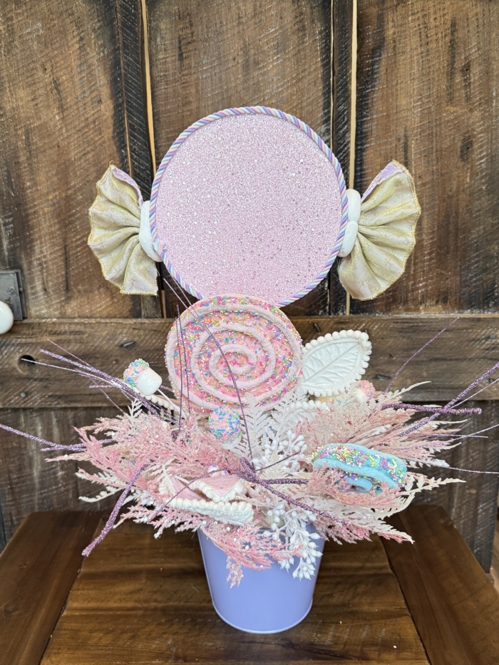 Back view of a whimsical candy centerpiece showcasing oversized candy decorations, pastel swirl lollipops, glitter details and decorative foliage.