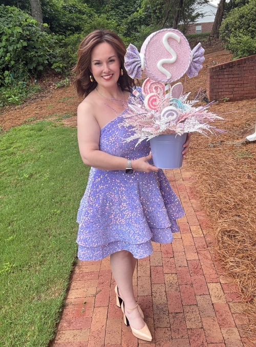 Designer holding a pastel candy party centerpiece with oversized candy decorations, glitter accents, and whimsical sweet shop details.