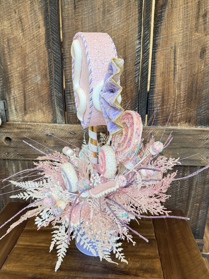 Pastel candy party centerpiece with faux candy swirls, sprinkle-covered sweets, glitter sprays, and frosted pink foliage viewed from the side.