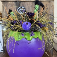 Back view of the handcrafted Witch's Brew centerpiece featuring purple pumpkin, florals, cascading greenery, and whimsical witch legs.