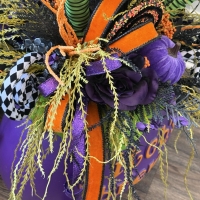 Close up of designer ribbon, purple rose, black and white harlequin curl spray, cascading greenery on witch's brew centerpiece.