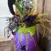 Angled view of the Witch's Brew Halloween centerpiece highlighting striped witch legs, spiderweb cauldron, florals, and whimsical Halloween accents.