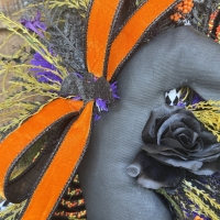Close up of premium orange velvet ribbon, black rose, and whimsical Halloween accents on a handmade witch swag.