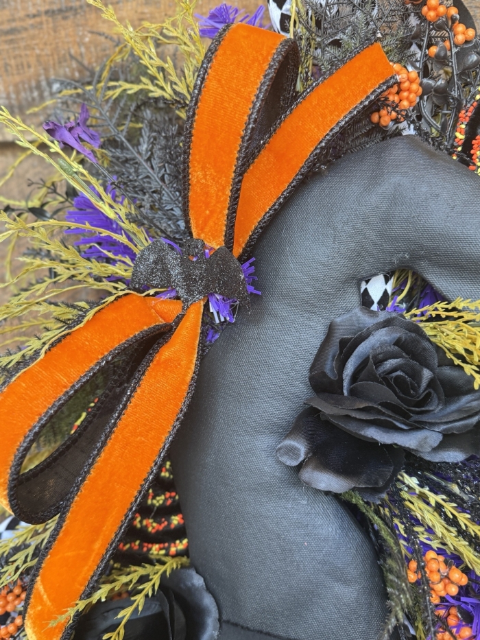 Close up of premium orange velvet ribbon, black rose, and whimsical Halloween accents on a handmade witch swag.