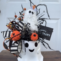 Whimsical Halloween ghost bucket centerpiece with orange pumpkins, black and white striped ribbon, candy corn ribbon, spooky black greenery and a fluffy ghost accent
