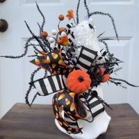Side view of a handcrafted Halloween ghost bucket arrangement featuring orange pumpkins, candy corn accents, striped ribbon, and wispy black Halloween greenery.
