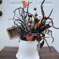 Back view of the Halloween ghost bucket centerpiece showing layered black greenery, candy corn picks, orange pumpkin accents and decorative ribbon details.
