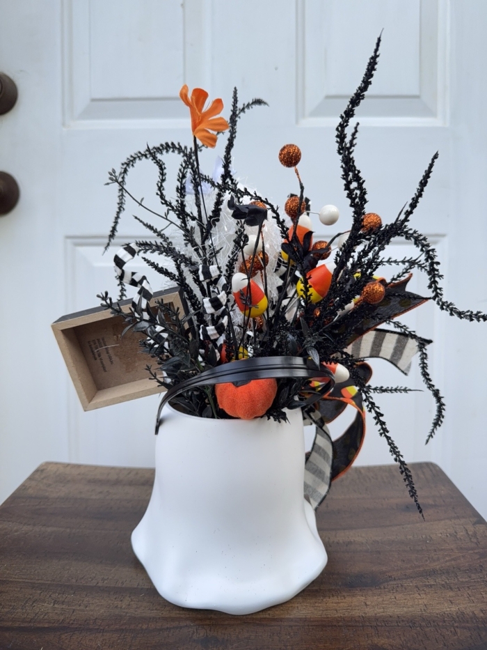 Back view of the Halloween ghost bucket centerpiece showing layered black greenery, candy corn picks, orange pumpkin accents and decorative ribbon details.